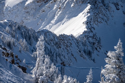 Snow-covered mountains with steep slopes and frosted trees under a clear blue sky.