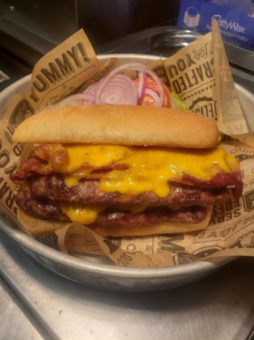 A hearty burger with multiple beef patties, melted cheese, crispy bacon, and sliced onions on a toasted bun, served with salad.