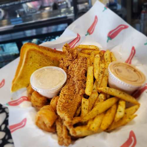 A plate of crispy chicken tenders, seasoned fries, toast, and two dipping sauces on a red and white patterned paper.