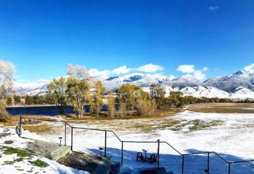 A snowy landscape with mountains in the background, trees with autumn leaves, and a clear blue sky.