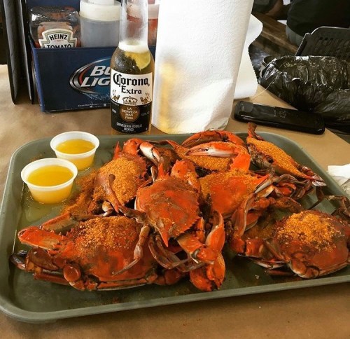 A tray of seasoned crabs with two dipping sauces, accompanied by a bottle of Corona beer and a paper towel.