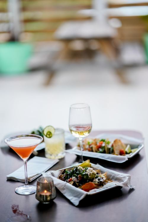 A table setting with two plates of colorful food, a cocktail, and a glass of white wine, with a blurred background.
