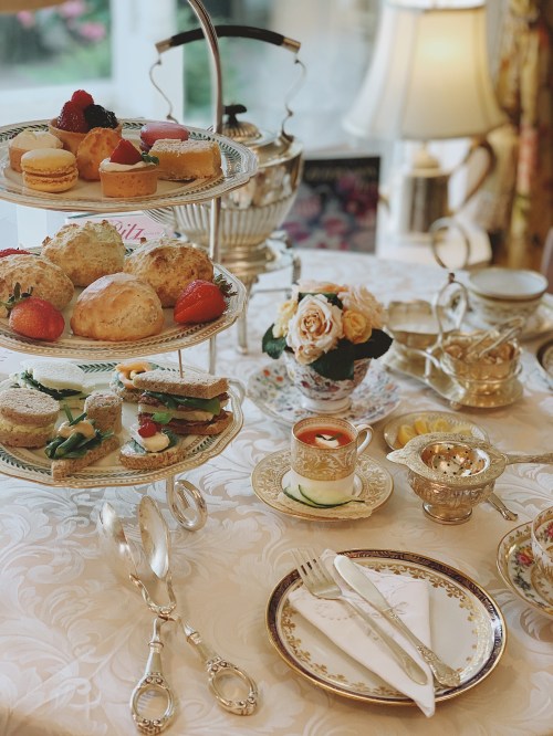 A beautifully arranged afternoon tea set with pastries, scones, sandwiches, and a floral centerpiece on an elegant table.