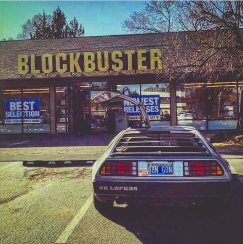 A DeLorean parked outside a Blockbuster store, with the sign prominently displayed in the background.