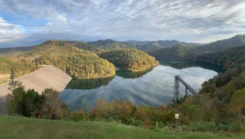 A scenic view of a reservoir surrounded by autumn-colored hills and mountains under a cloudy sky.