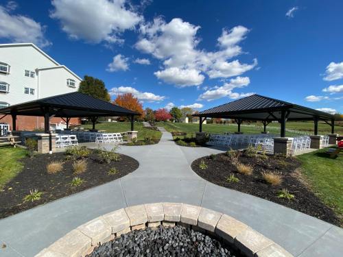 Two pavilions with chairs set up for an event, surrounded by landscaped paths and colorful autumn trees under a blue sky.