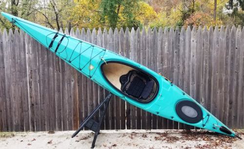 A turquoise kayak is propped up against a wooden fence, showcasing its sleek design and interior.
