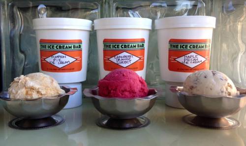 Three ice cream flavors in metal bowls: pumpkin pie, cranberry sorbet, and maple pecan, with tubs in the background.