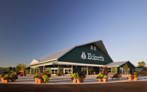 A green barn-style building with the Eckert's logo, surrounded by potted plants and a clear blue sky.