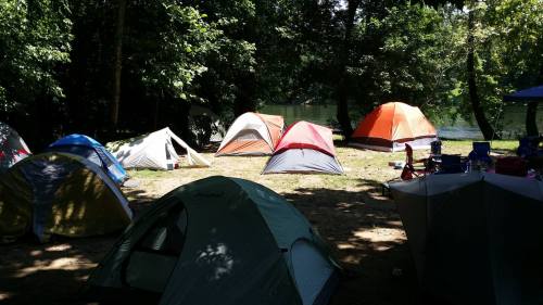 A campsite with several colorful tents set up near a river, surrounded by trees and greenery.