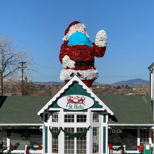 A large, festive Santa Claus wearing a blue mask stands on the roof of a building decorated for the holidays.