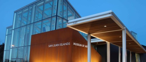Modern glass and metal building of the San Juan Islands Museum of Art, illuminated at dusk.