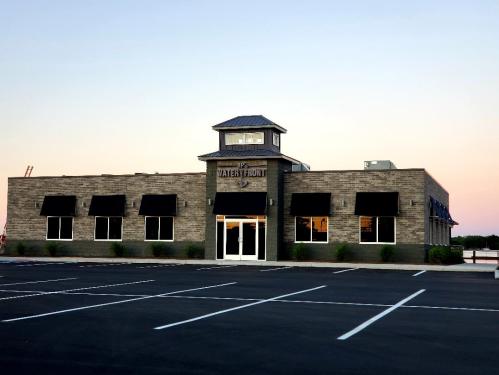 A modern building with a tower, large windows, and a parking lot, set against a sunset sky.