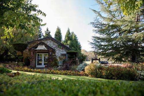 A charming stone building surrounded by lush greenery and colorful flowers under a clear blue sky.