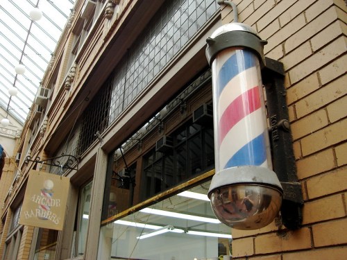 A vintage barber pole with red, white, and blue stripes outside a barbershop in a brick building.