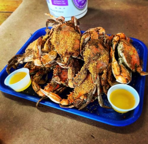 A blue tray filled with seasoned crabs and two small cups of dipping sauce.