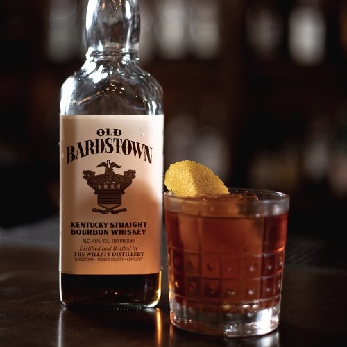 A bottle of Old Bardstown Kentucky Straight Bourbon Whiskey next to a glass of whiskey garnished with a lemon twist.
