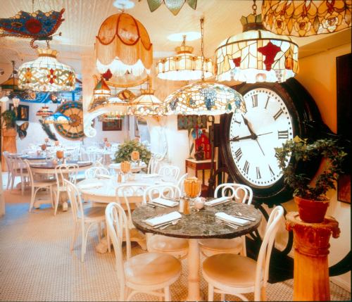 A cozy restaurant interior featuring ornate stained glass lamps, round tables, and a large clock on the wall.