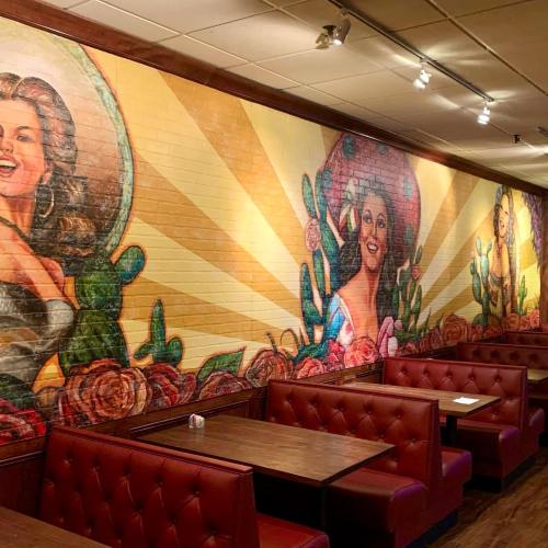 Colorful mural of women surrounded by flowers and cacti, with red booths and wooden tables in a cozy restaurant setting.
