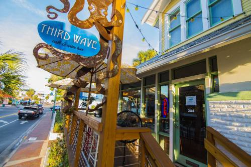 Sign for "Third Wave Café & Wine Bar" with an octopus design, located on a sunny street with outdoor seating.