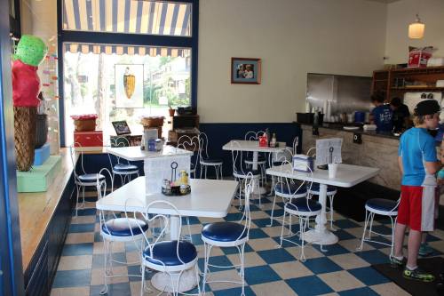 Bright ice cream shop interior with blue and white decor, featuring tables, chairs, and a counter with staff.