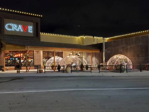 Outdoor dining area with illuminated geodesic domes in front of a restaurant named "CRAVE" at night.