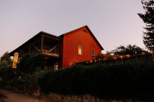 A charming red hotel building at dusk, adorned with string lights and surrounded by lush greenery.