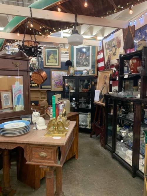 A cozy antique shop filled with vintage furniture, artwork, and collectibles, illuminated by warm string lights.