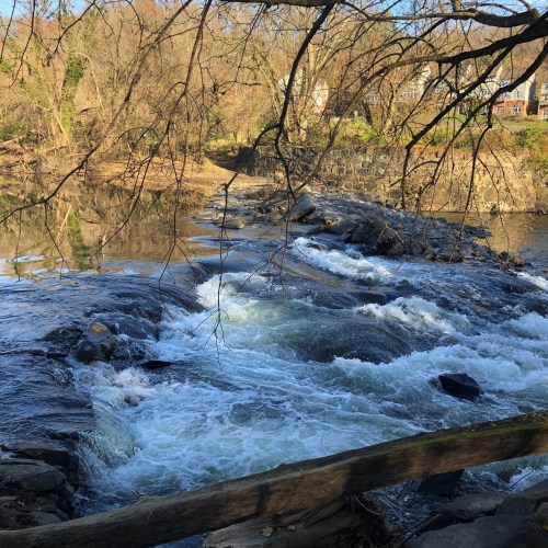 A serene river scene with flowing water, rocks, and trees, reflecting a peaceful natural landscape.