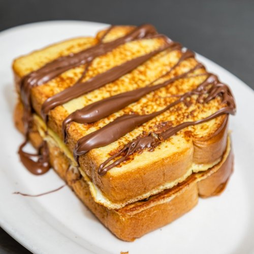 A stack of golden-brown French toast drizzled with chocolate sauce on a white plate.