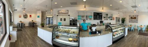 A bright bakery interior with a display case, seating area, and a staff member in a blue shirt behind the counter.