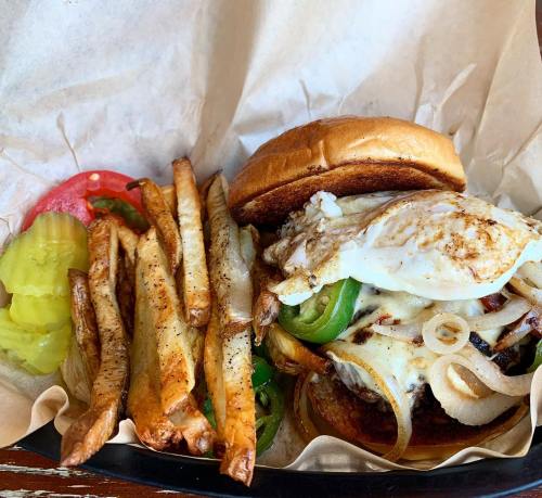 A juicy burger topped with cheese, onions, and a fried egg, served with crispy fries and pickles on the side.