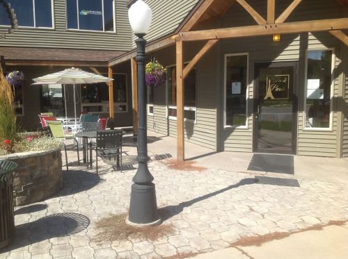 A sunny outdoor area with a lamp post, patio furniture, and flower planters near a building entrance.