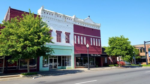 Historic buildings with colorful facades and trees lining a sunny street.