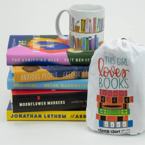 A stack of colorful books with a mug and a sleep shirt bag featuring a book design, celebrating a love for reading.