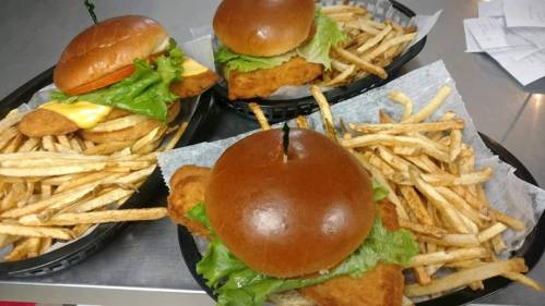 Three baskets of sandwiches with fried chicken, lettuce, and cheese, served with a side of crispy French fries.