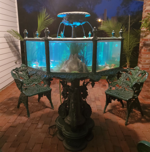 A decorative fish tank with a fountain, surrounded by two green chairs, set in a dimly lit outdoor area.