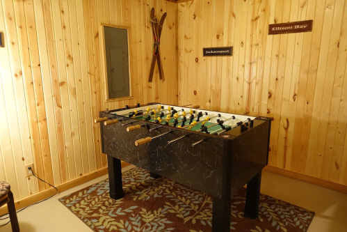 A foosball table in a wooden room with a patterned rug and wall signs.