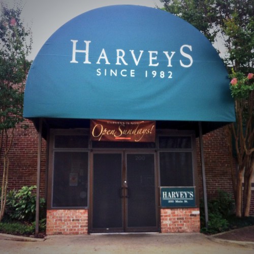 Storefront of Harveys with a green awning, "Open Sundays" sign, and brick facade. Established in 1982.