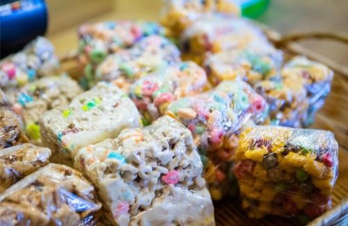 Colorful, wrapped rice crispy treats stacked on a wooden surface, featuring various toppings and textures.