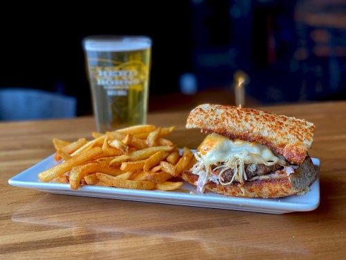 A delicious sandwich with melted cheese and pulled meat, served with golden fries and a pint of beer on a wooden table.