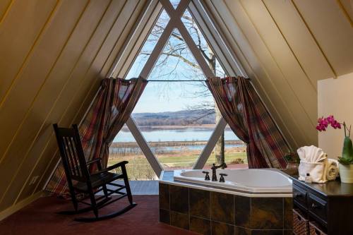 Cozy bathroom with a large window overlooking a scenic lake, featuring a rocking chair and a stylish bathtub.