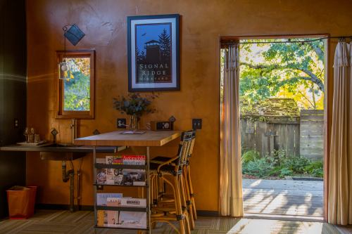 Cozy interior with a wooden bar, magazines, and a view of a garden through an open door. Warm, inviting atmosphere.