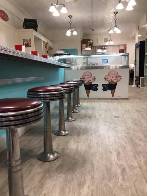 A retro diner interior featuring a long counter and red leather stools, with ice cream cone decorations on the wall.