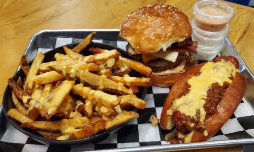 A plate with a burger topped with cheese and bacon, a hot dog with cheese, and a side of crispy fries.