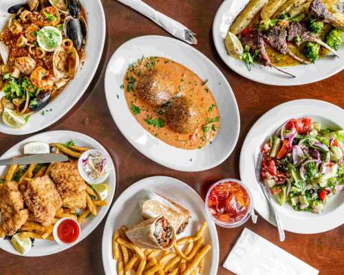 A spread of various dishes including seafood, salad, fried fish, and a wrap, all served on white plates.
