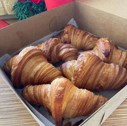 A box filled with freshly baked, golden-brown croissants arranged neatly on parchment paper.