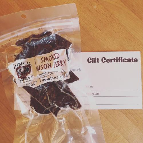 A package of smoked bison jerky next to a blank gift certificate on a wooden surface.