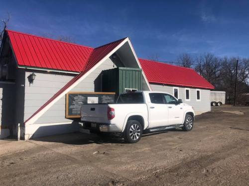 A white truck parked beside a building with a red roof and green accents on a clear day.