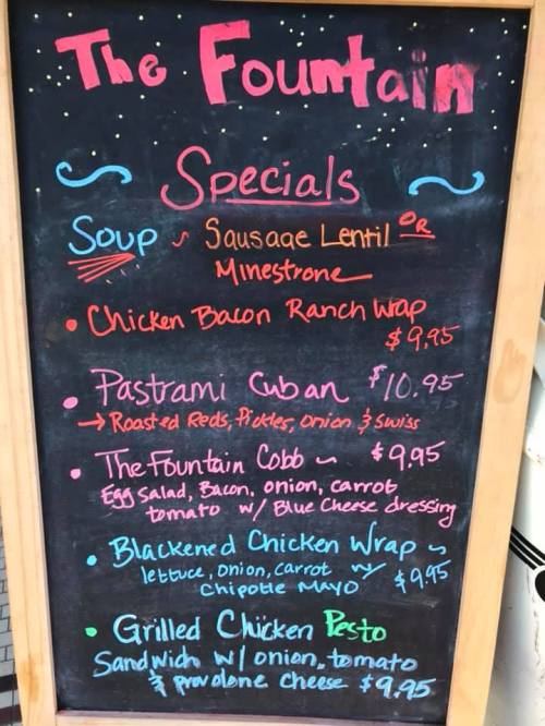 Chalkboard menu listing daily specials: soups, wraps, and sandwiches with prices. Colorful design with decorative elements.